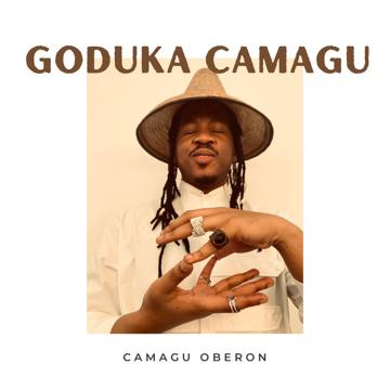 A person wearing a wide-brimmed hat and white shirt poses with closed eyes and hands gesturing in front of them. The large text above reads "GODUKA CAMAGU" and below in smaller text is "CAMAGU OBERON", all on a plain background.